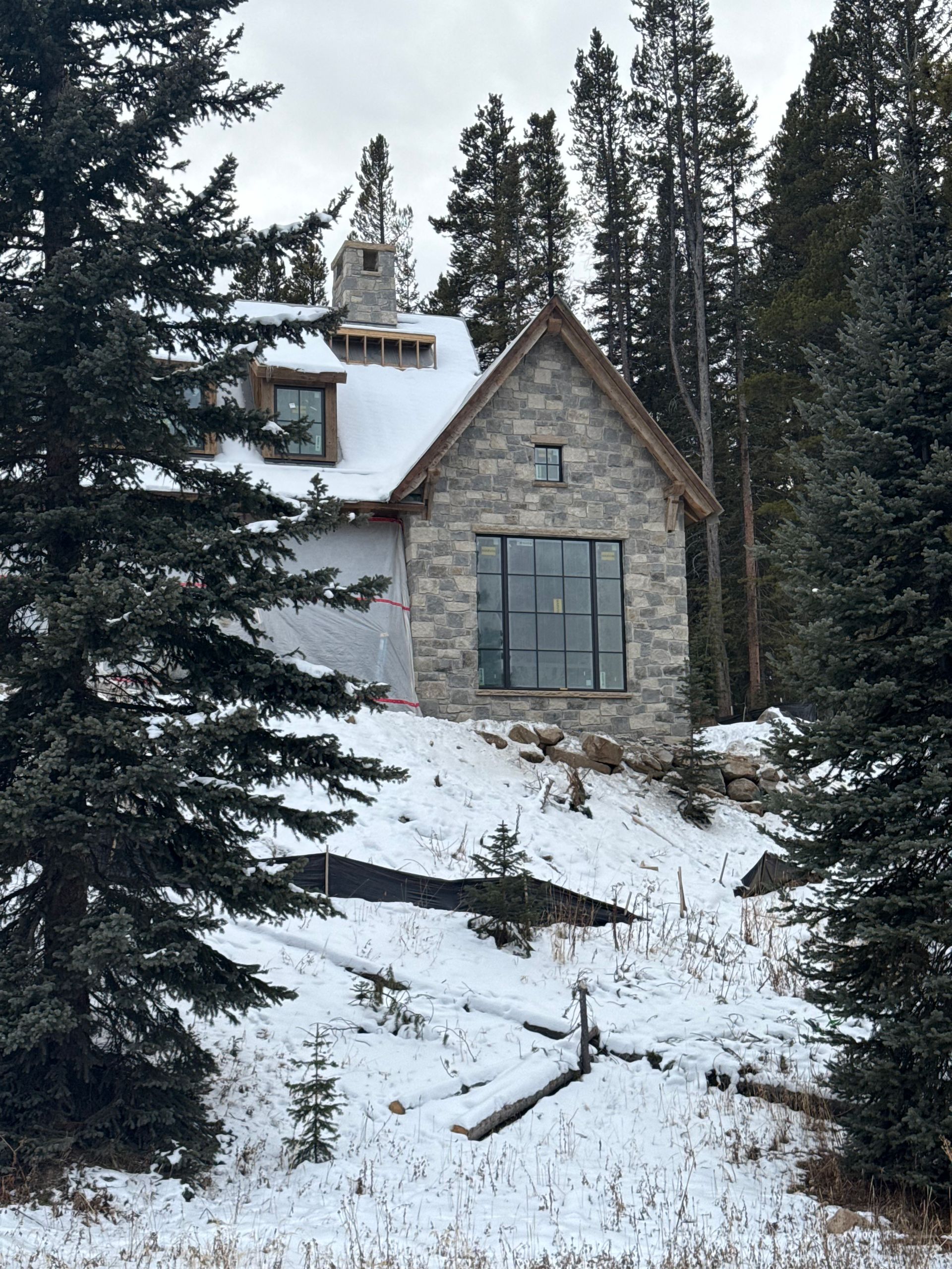 Stone house with large window in a snowy, wooded area.