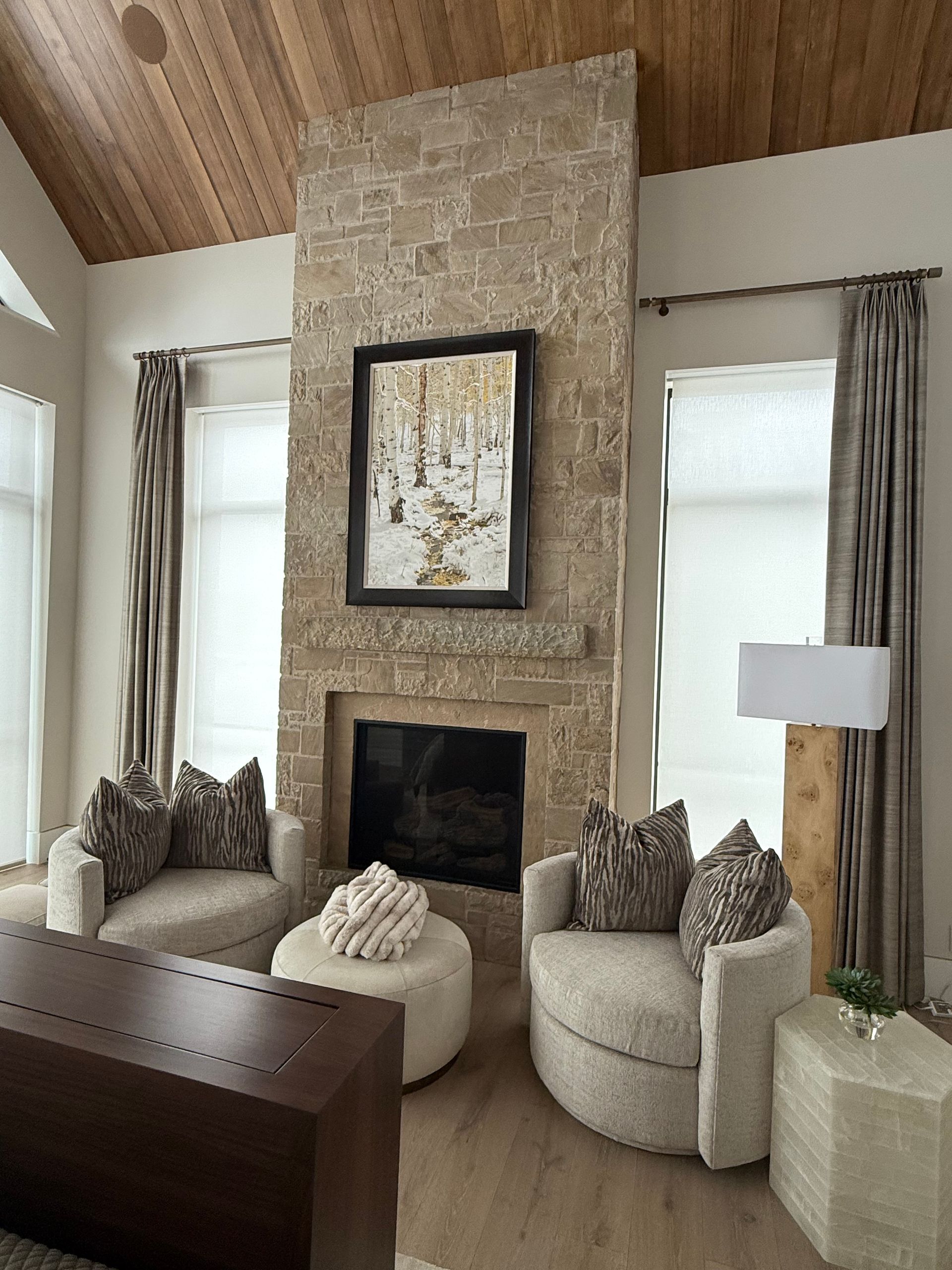 Cozy living room with stone fireplace, artwork, two armchairs, and wood-beam ceiling.