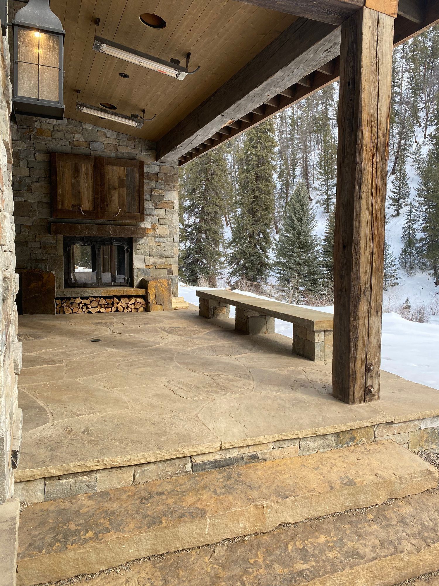 a stone porch with a fireplace and benches in the snow .
