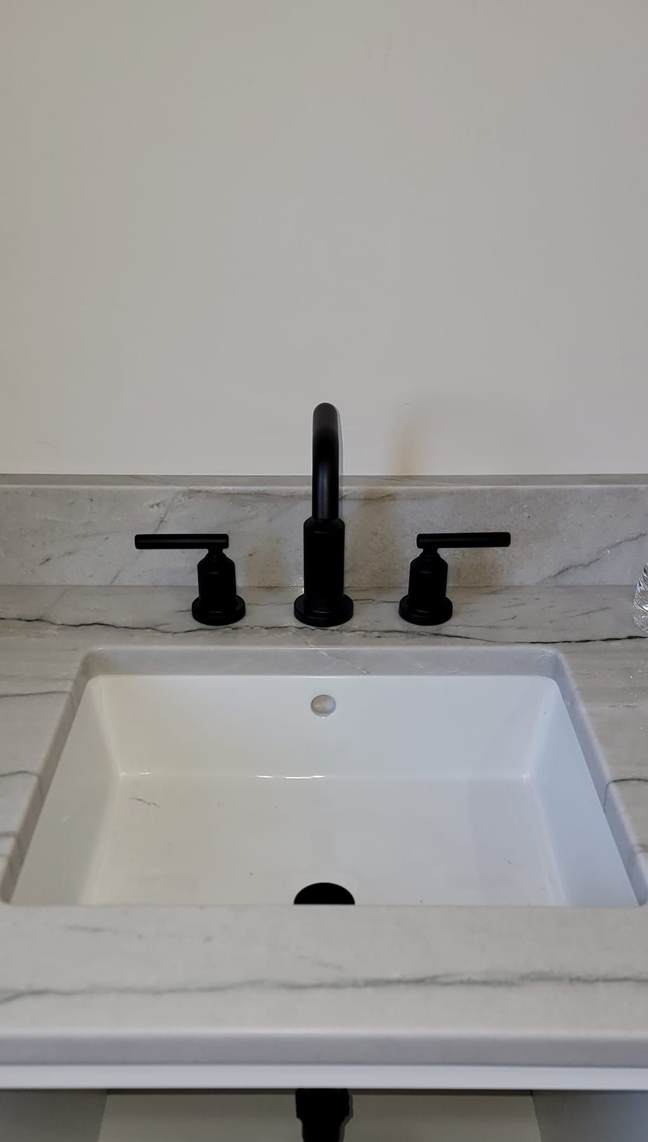 A modern white bathroom sink with a matte black three-piece faucet fixture set against a white marble countertop.