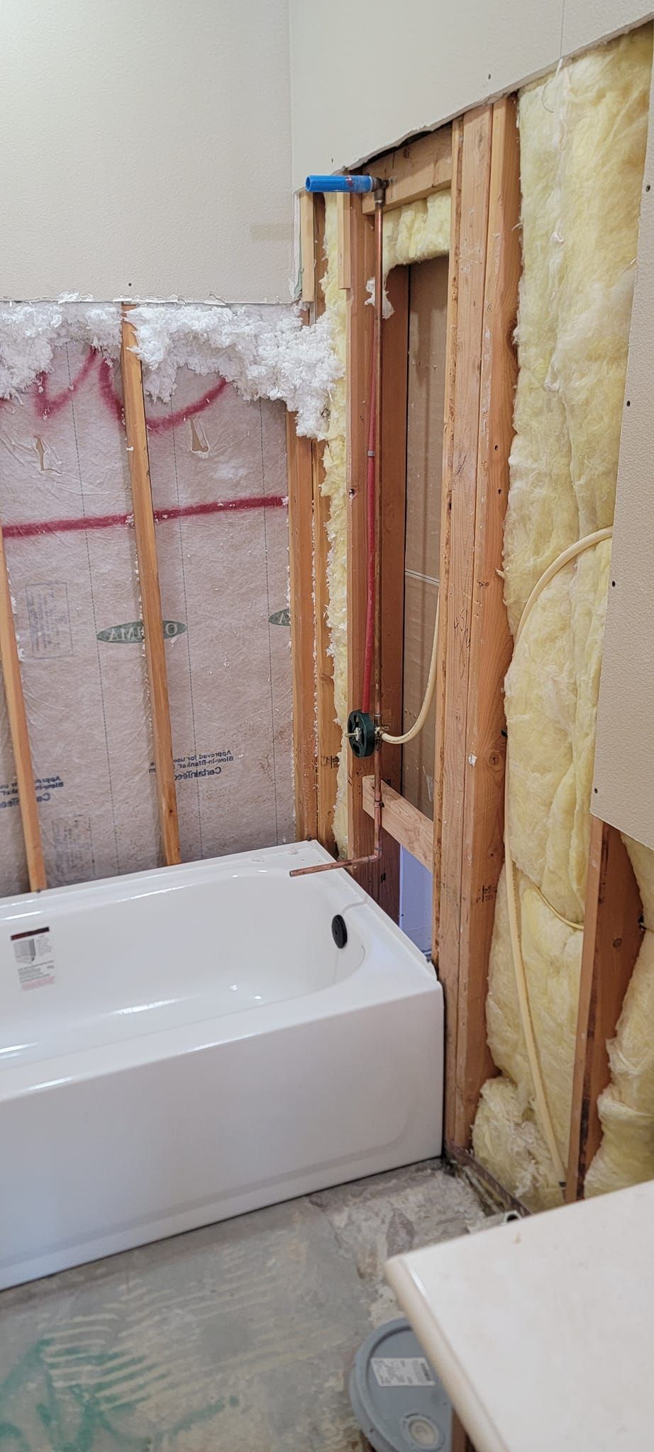 A bathroom under construction featuring a white bathtub, exposed wall studs, and insulation.