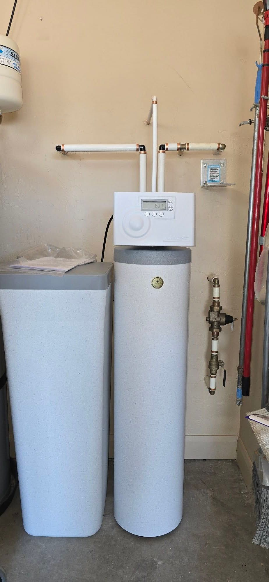 A water softener system featuring a tall, white mineral tank and a rectangular brine tank standing against a wall.