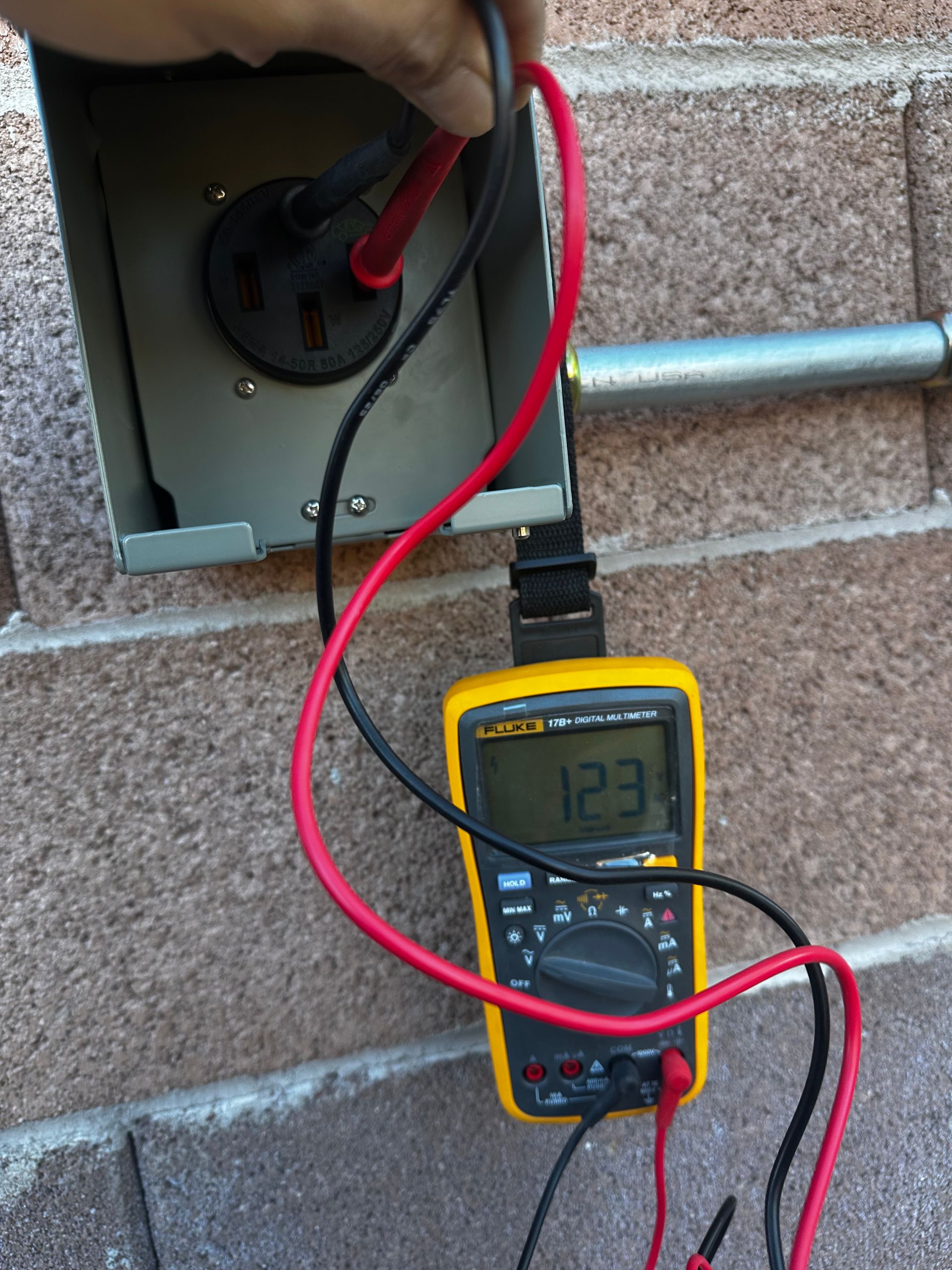 A person tests an outdoor outlet with a multimeter, reading 123 volts.