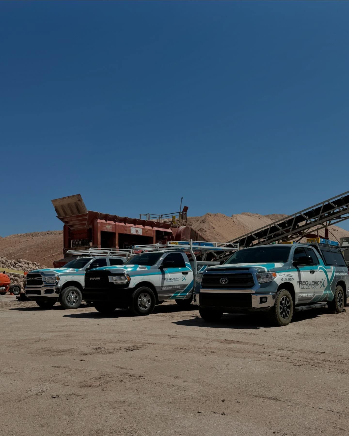 Four company trucks parked in front of an industrial facility under a blue sky.