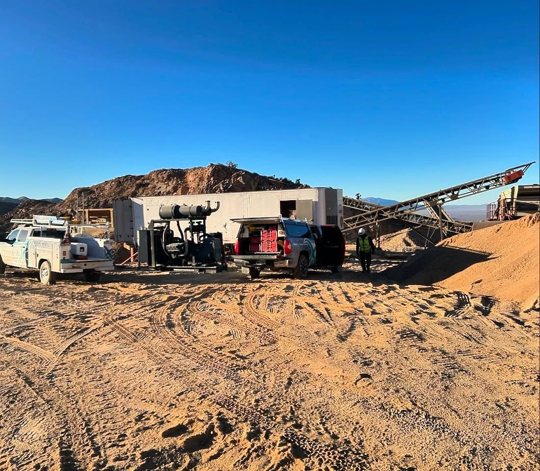 Vehicles and equipment at a construction site in a desert landscape under a clear blue sky.