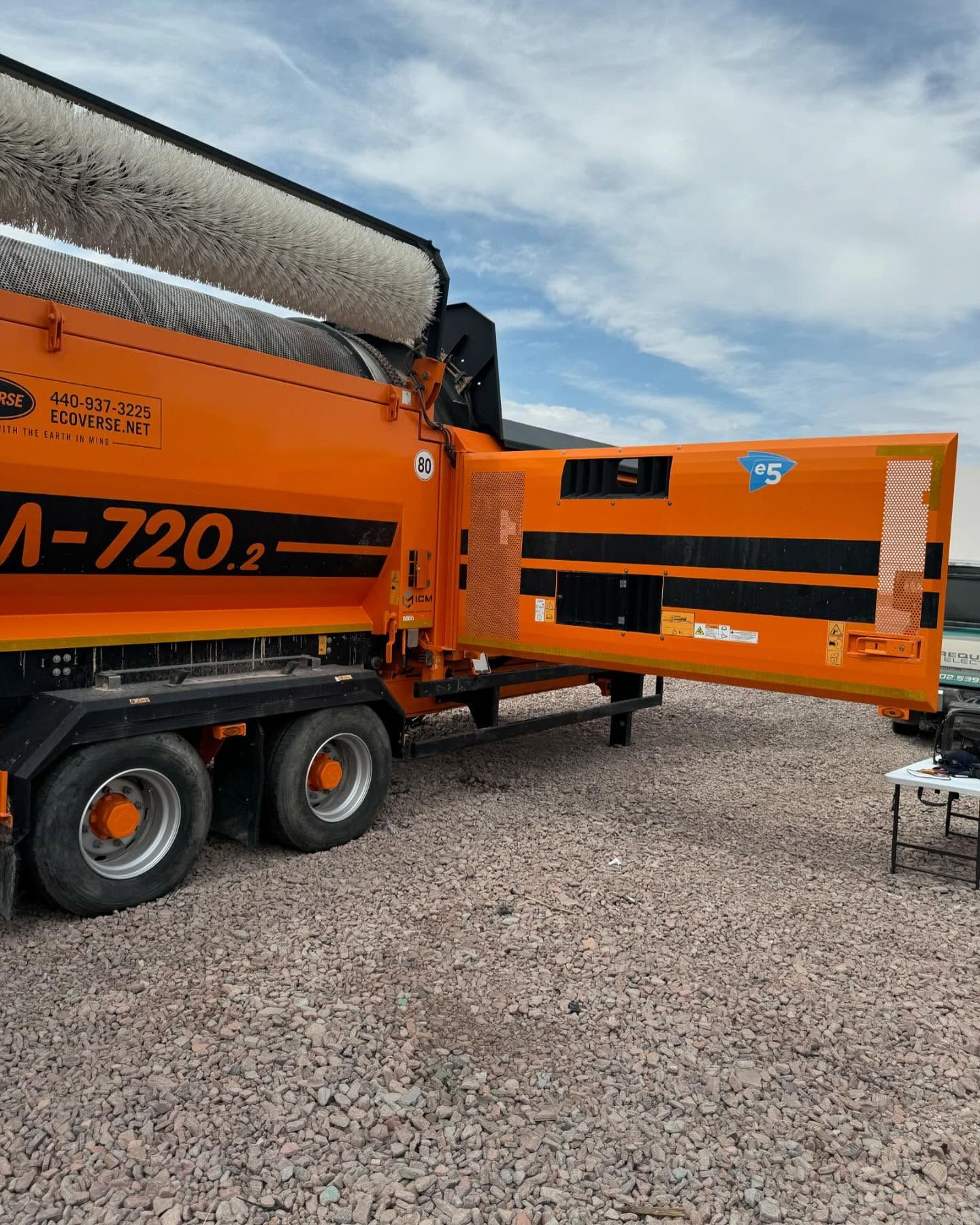 Orange industrial machine, likely for sweeping, parked outdoors on gravel.