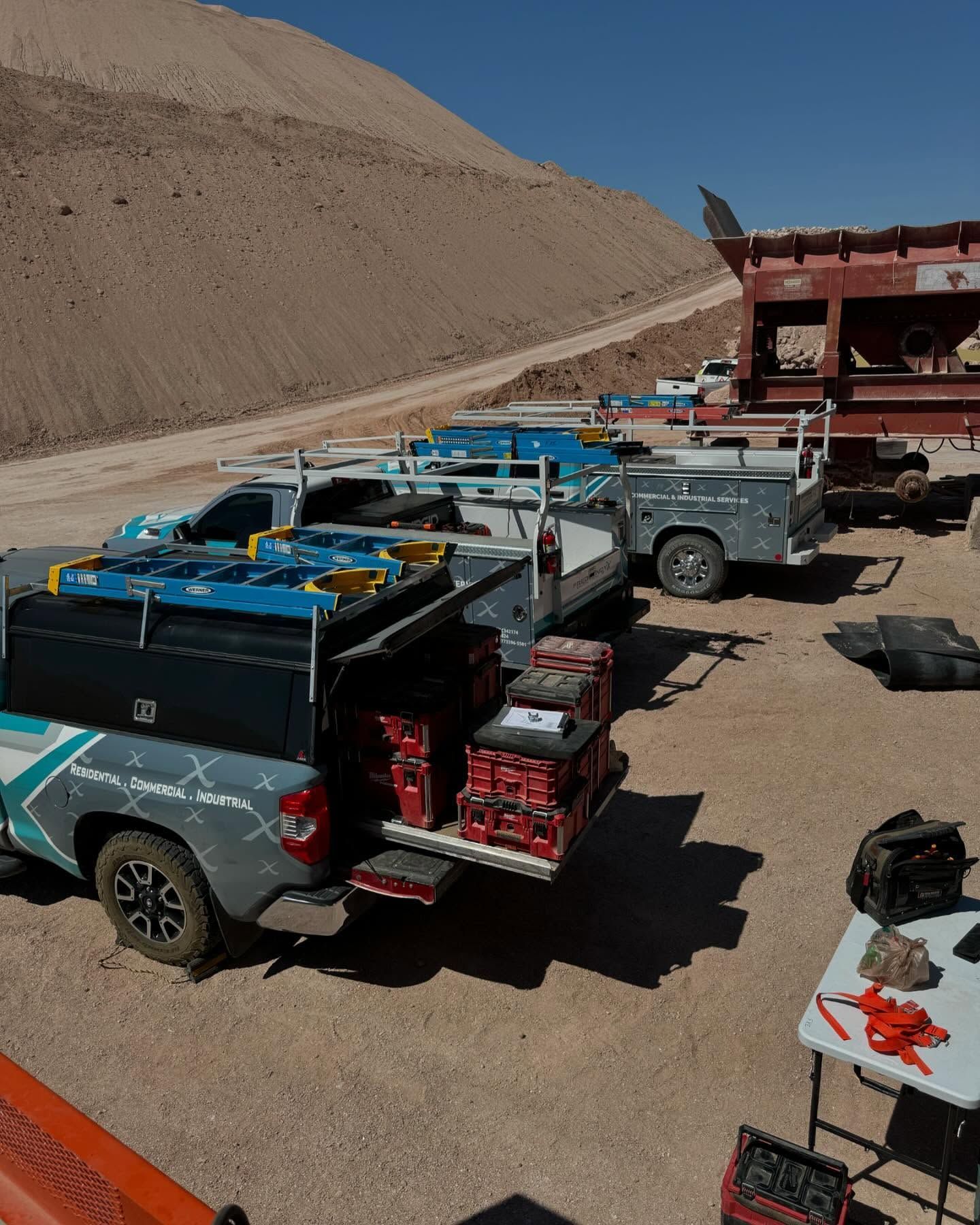 Work trucks loaded with equipment at a construction site, with a large dirt hill in the background.
