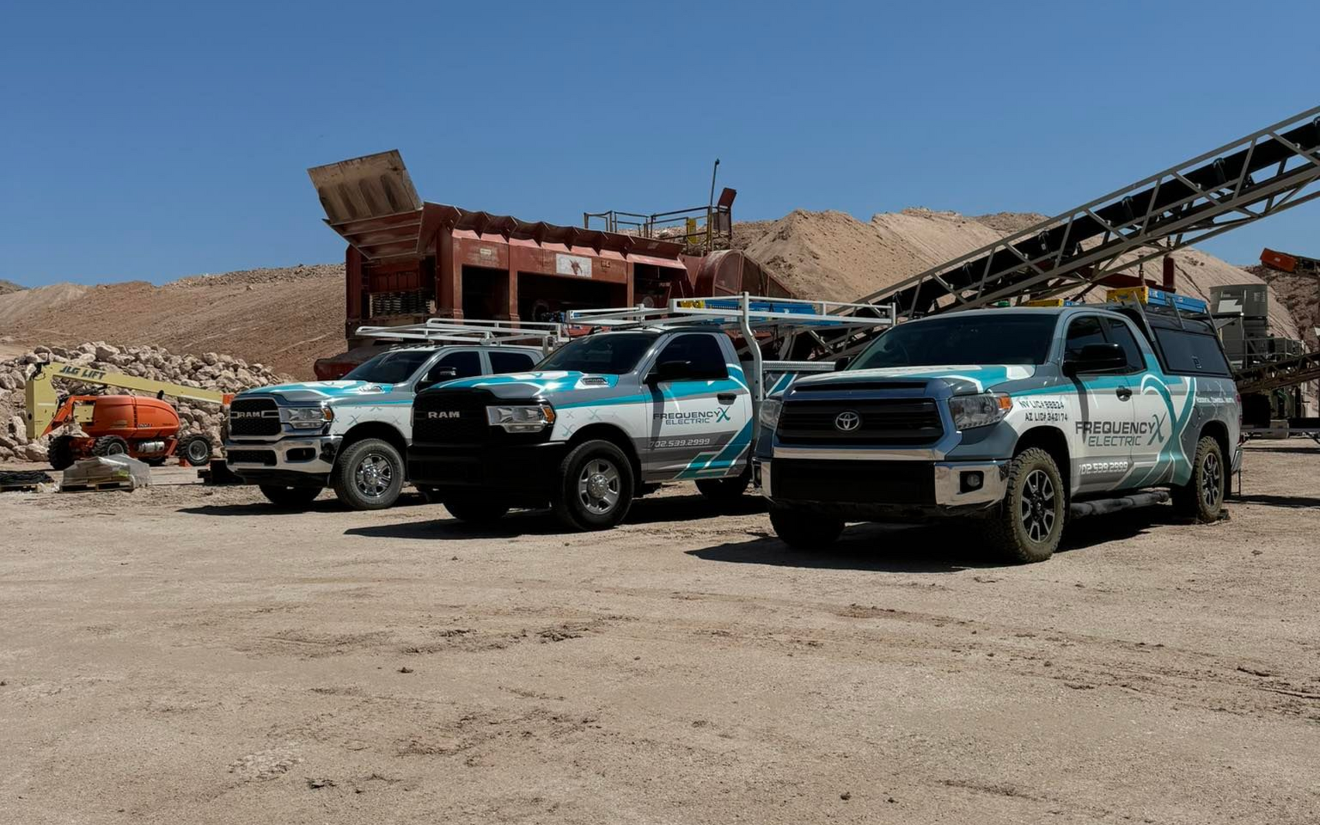 Three company trucks parked in a quarry on a sunny day.