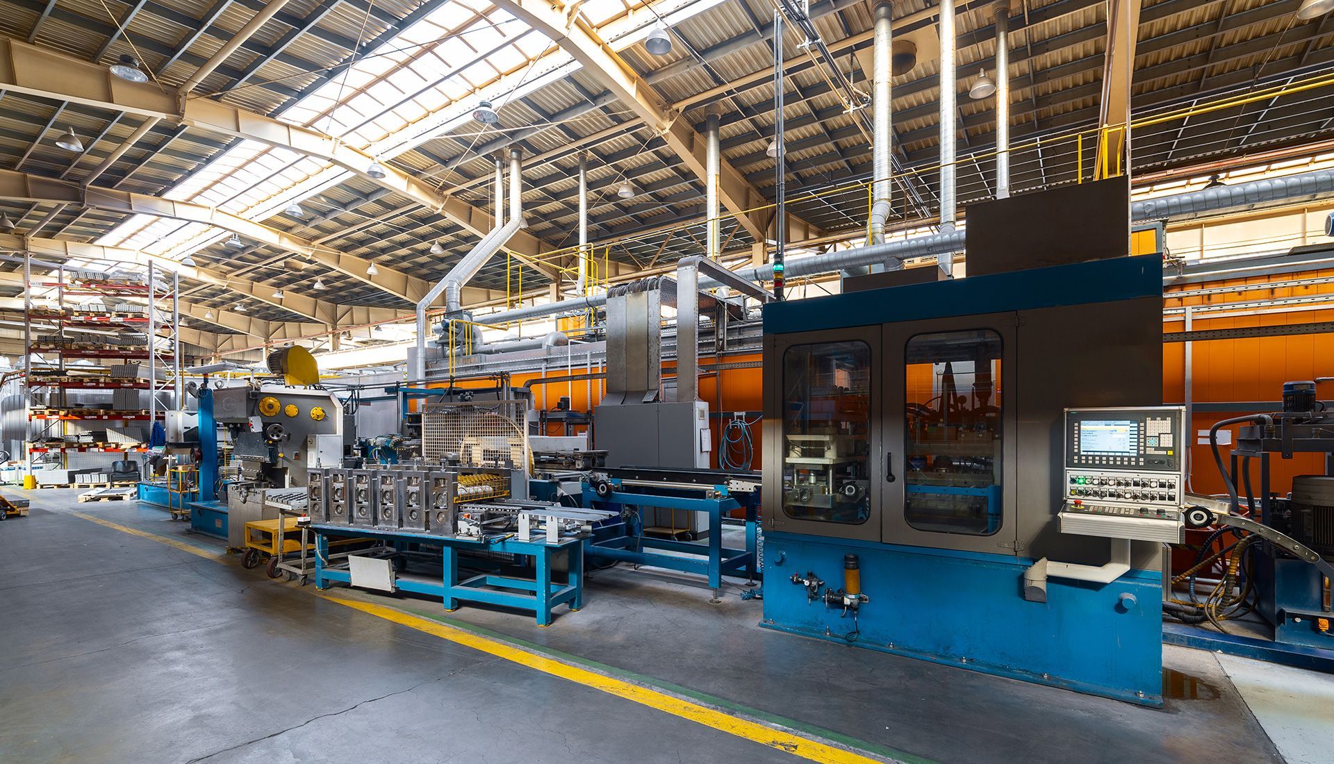 Factory interior with industrial machinery and control panel along a yellow line.