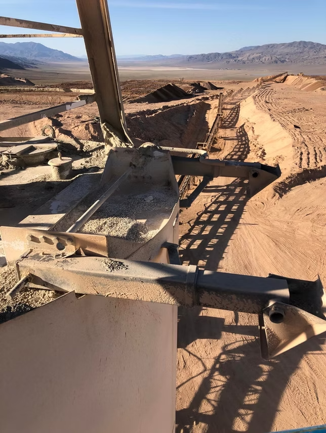 Desert landscape with industrial machinery, including conveyors, likely used for mining or processing materials.