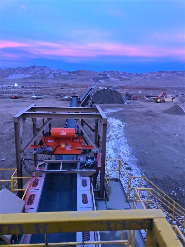 Industrial conveyor belt in a barren landscape under a dusky blue and pink sky.