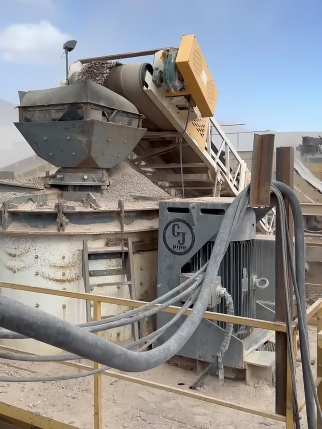 Industrial machinery: Rock crusher with conveyor belt, beige and grey, outdoors.