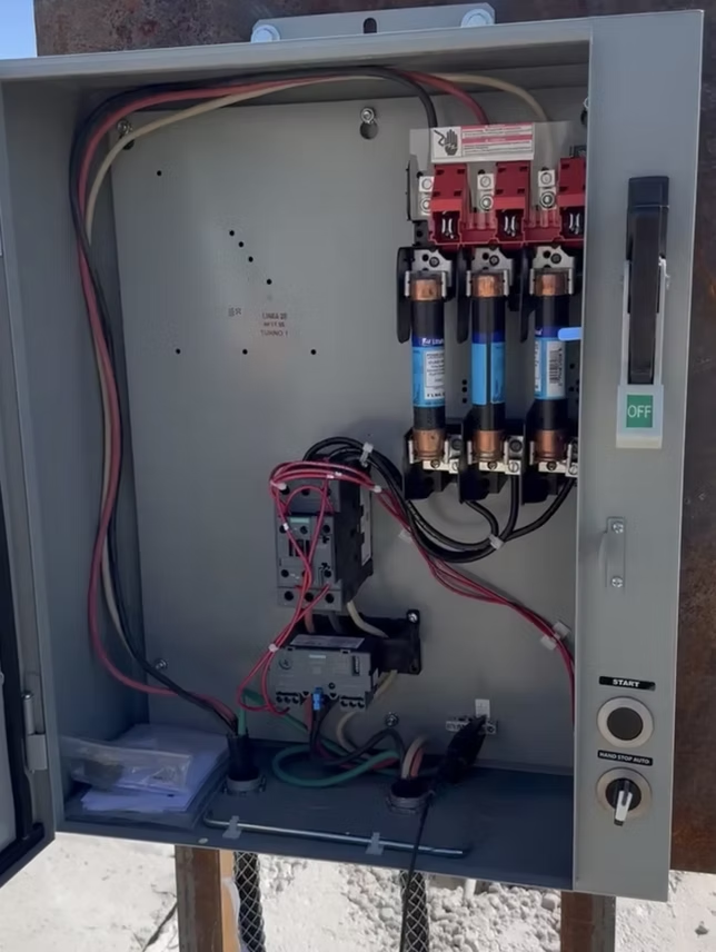 Open gray electrical panel with wires and circuit breakers.