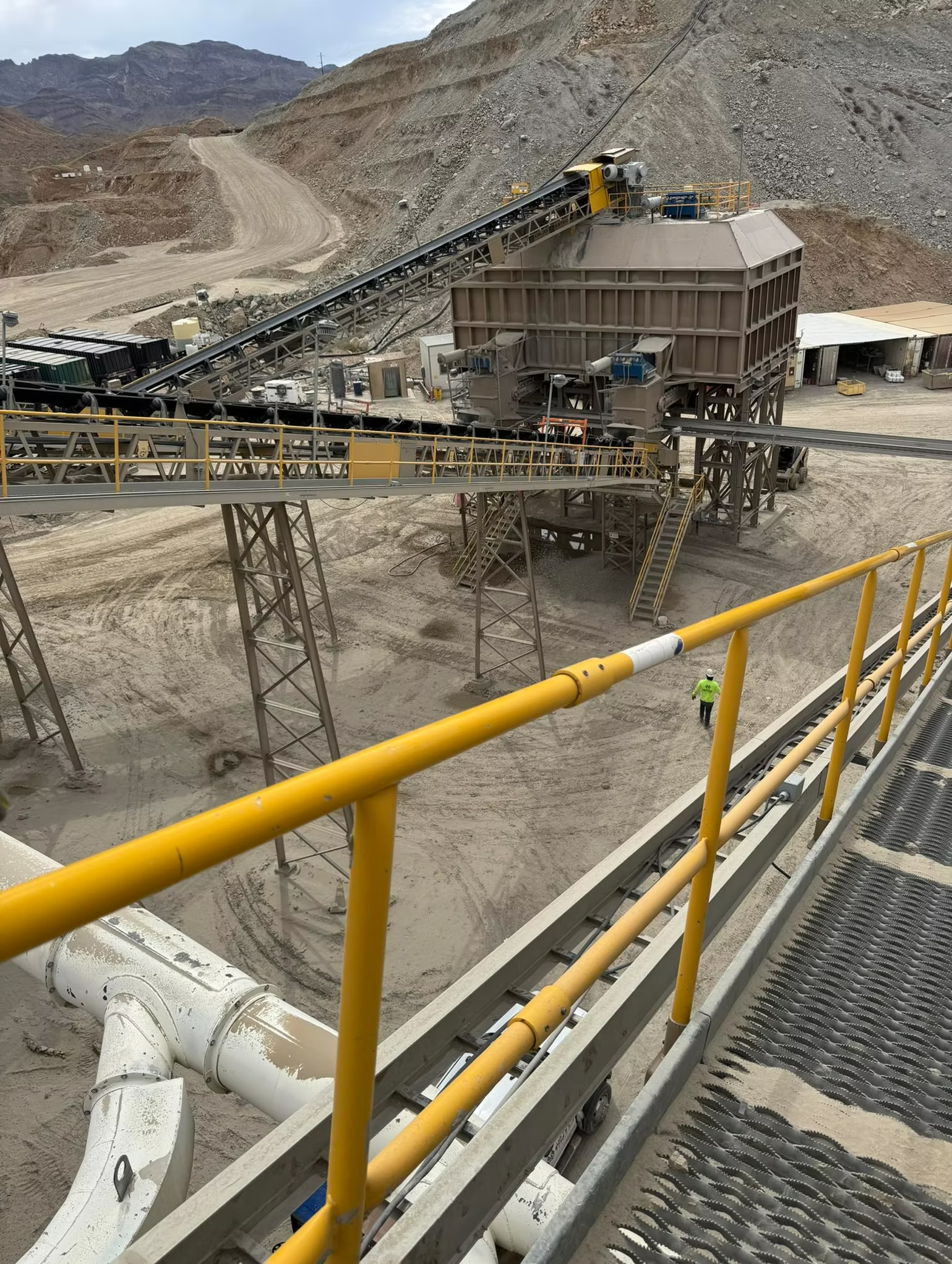 Mining operation with conveyor belts and processing equipment in a quarry, viewed from a yellow-railed walkway.