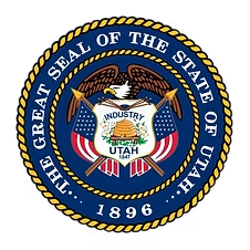 Utah state seal: Eagle above beehive, American flags, text, and date 1896, blue and gold.