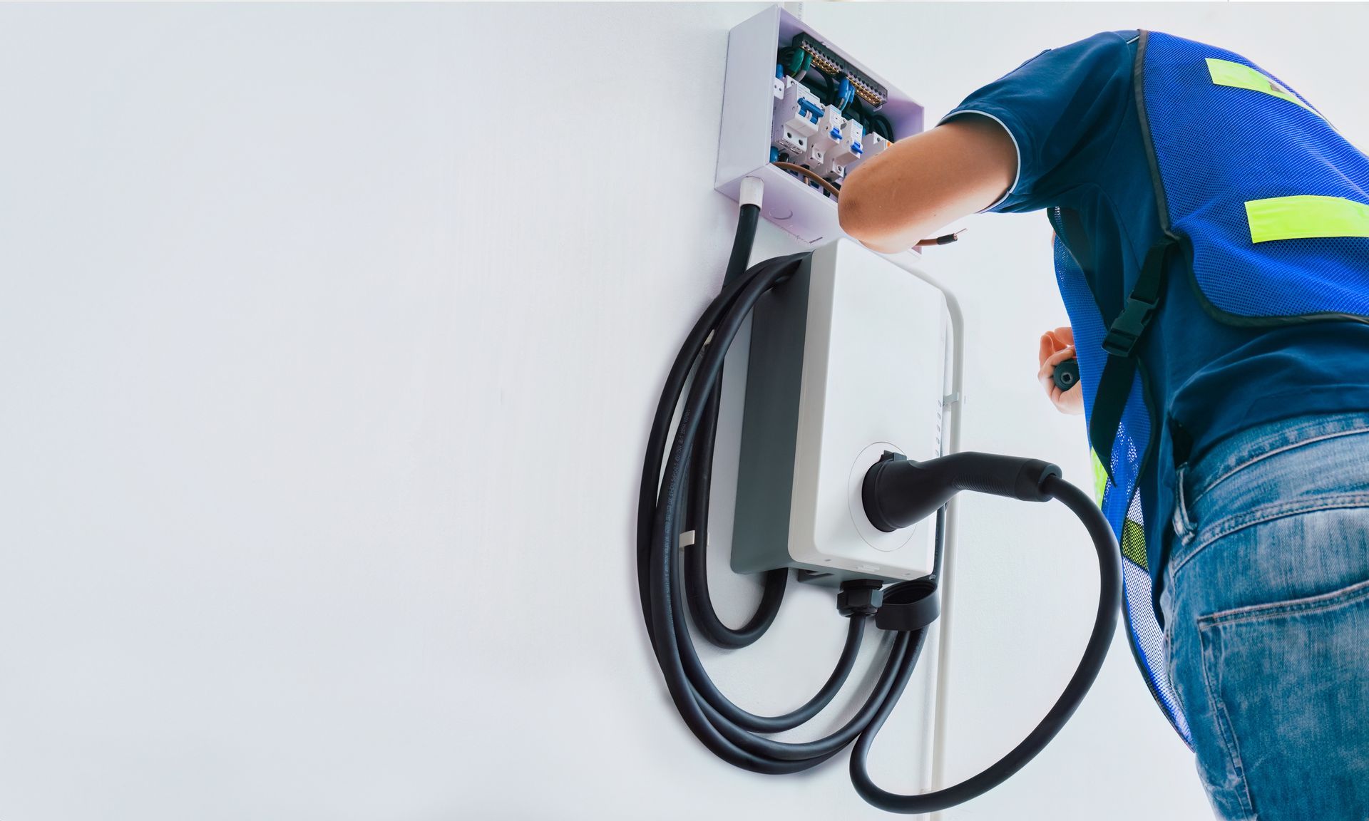 Electrician installing an electric vehicle charger on a white wall.