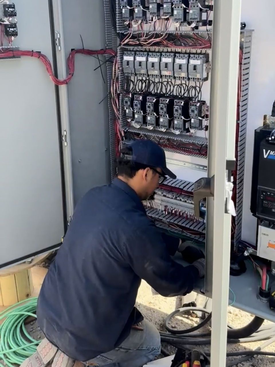 Person working on electrical panel, outdoors. Wires and components visible.