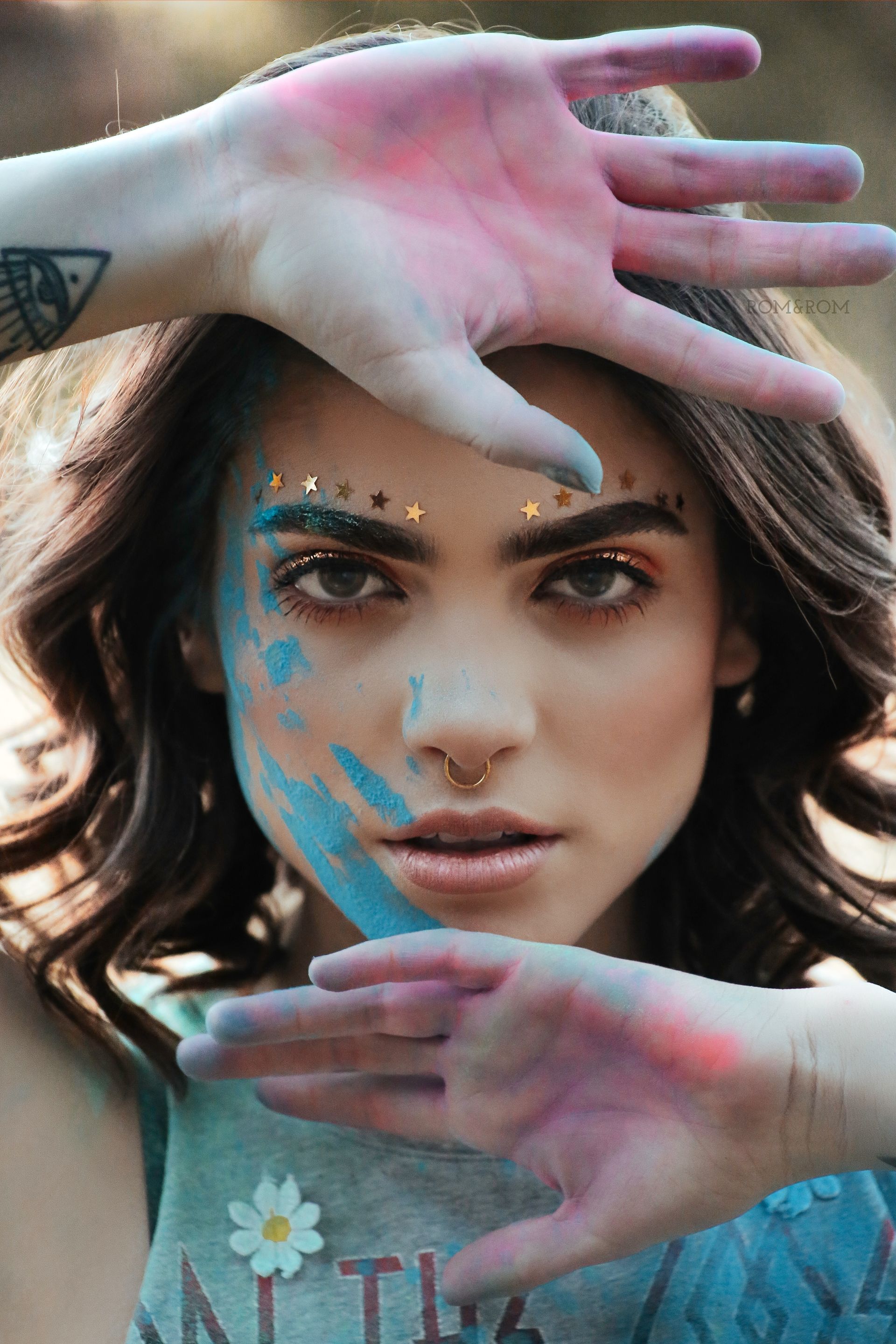 Mujer con pintura de colores en la cara y las manos, enmarcando el rostro, mirando a la cámara.Retrato profesional cinematográfico para marca personal realizado por RomRom.