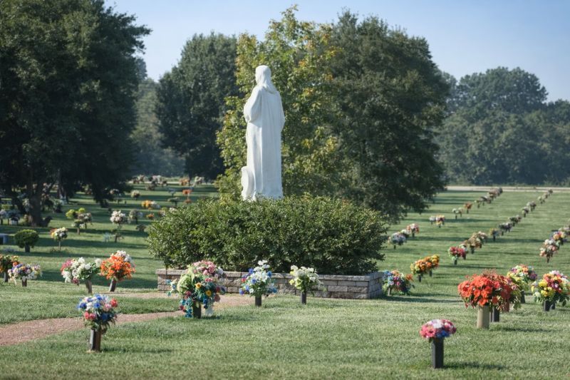 Columbia, TN Cemeteries lawn with white statue monument, green grounds and colorful grave flower arrangements.