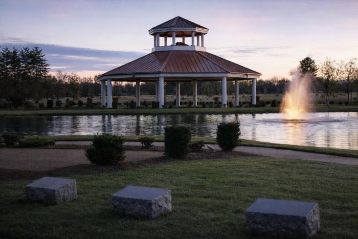 Columbia, TN cemeteries pavilion by pond with fountain at dusk, landscaped paths and granite markers.