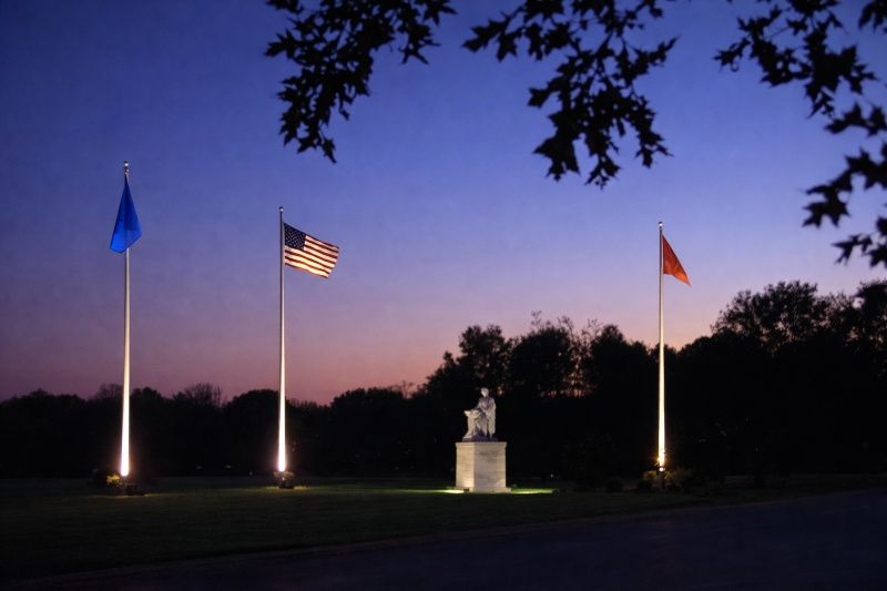 Summertown, TN Cemeteries twilight scene with lit flagpoles, U.S. flag and illuminated statue monument.