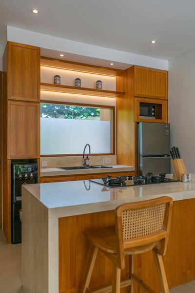 A kitchen with wooden cabinets , a stove , a refrigerator , a sink and a wicker chair.
