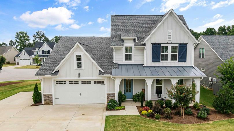 A white house with blue shutters and a gray roof is sitting on top of a lush green lawn.