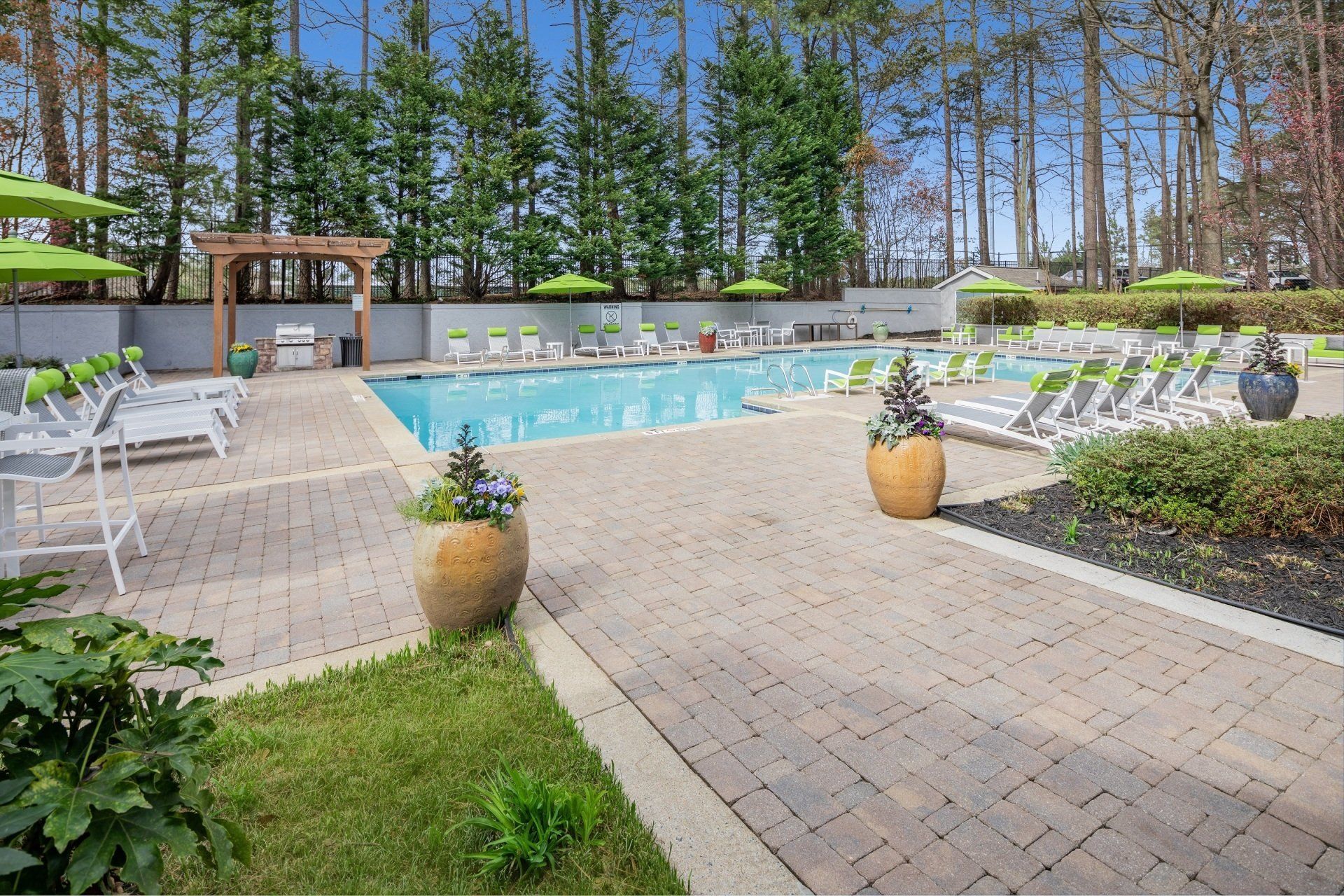 Pool area with lounge chairs, lime green umbrellas, and a barbecue under a pergola.