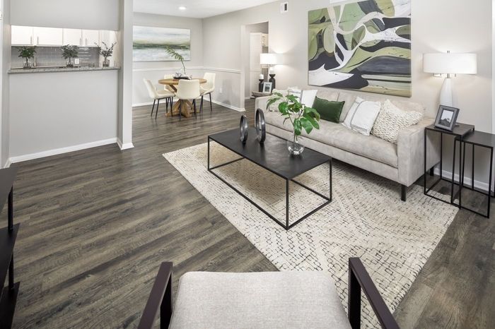 Living room with gray wood floors, beige sofa, black coffee table, and abstract art.