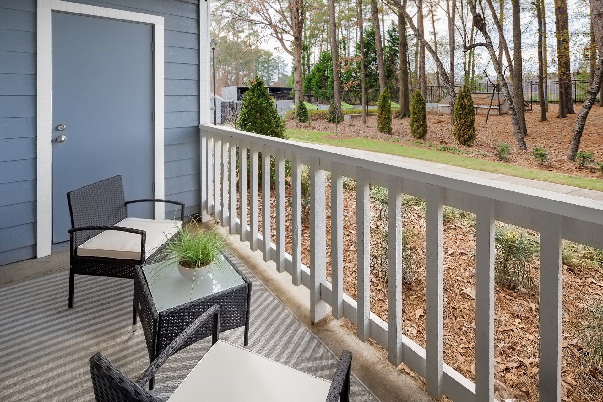 Patio with outdoor seating, light wood railing, and view of trees and foliage.
