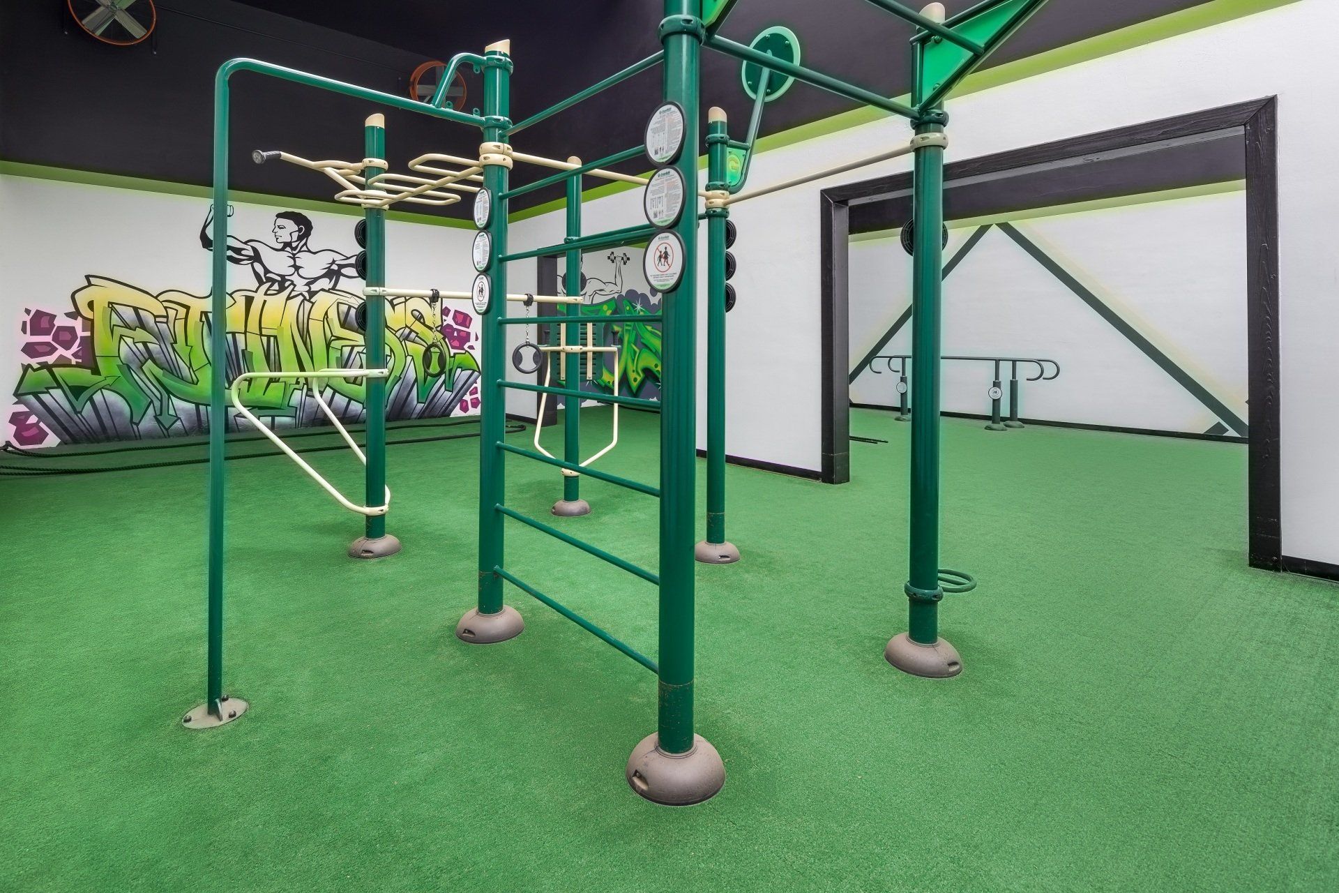 Green exercise equipment in a gym with graffiti, on green turf flooring.