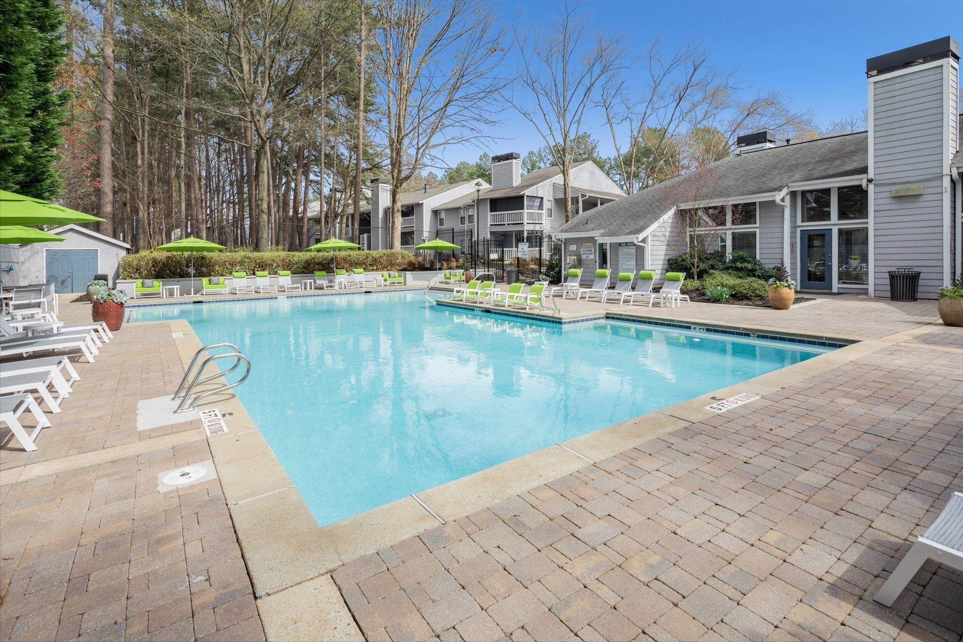 Swimming pool at an apartment complex; loungers, umbrellas, and a building in the background.