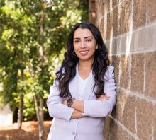 Anjabeen leaning against a brick wall with her arms crossed.