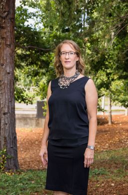 Arien, in a black top and skirt, is standing in front of a tree.