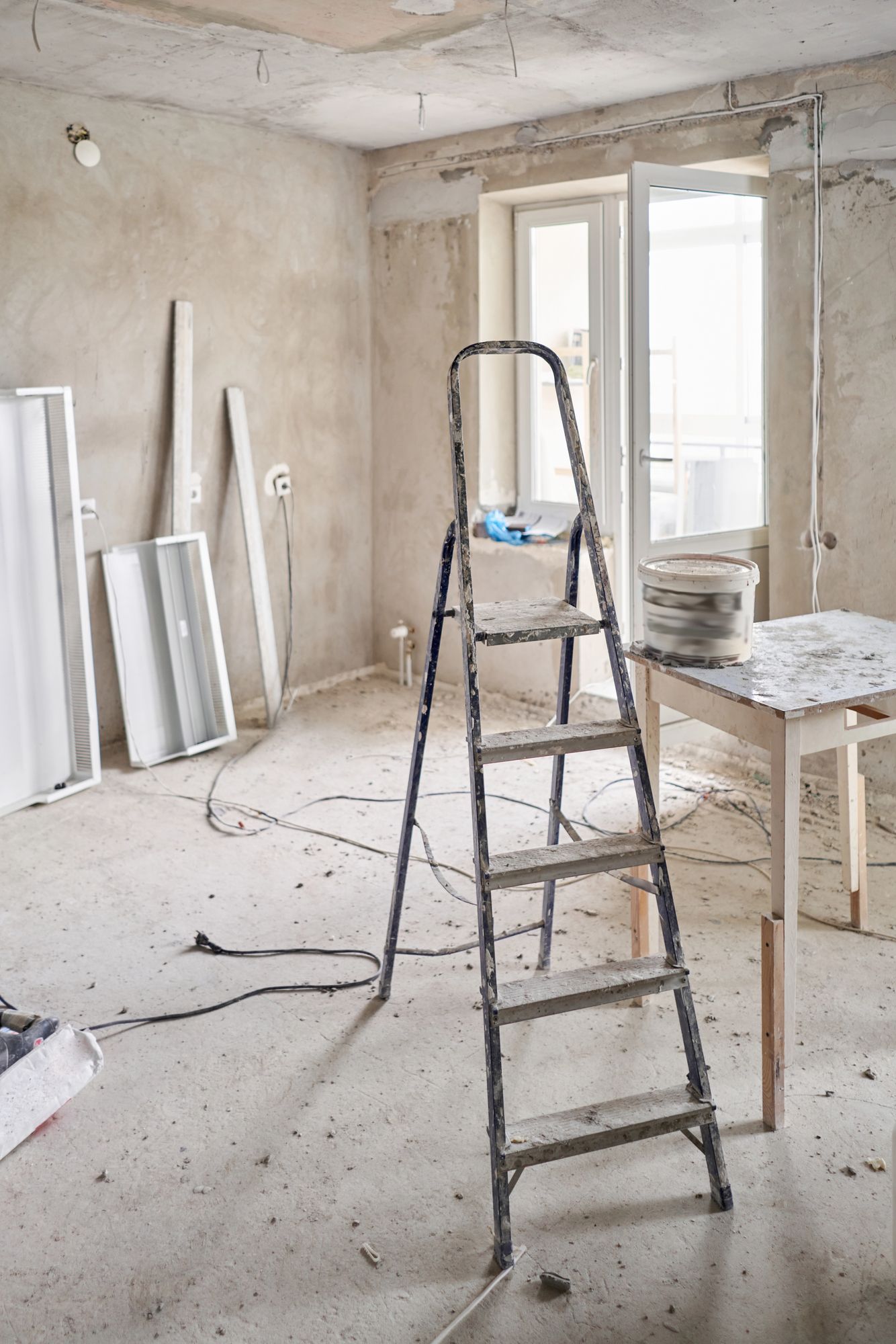 Stanza interna in fase di ristrutturazione; scala, finestra aperta, cavi elettrici esposti e materiali da costruzione sparsi.