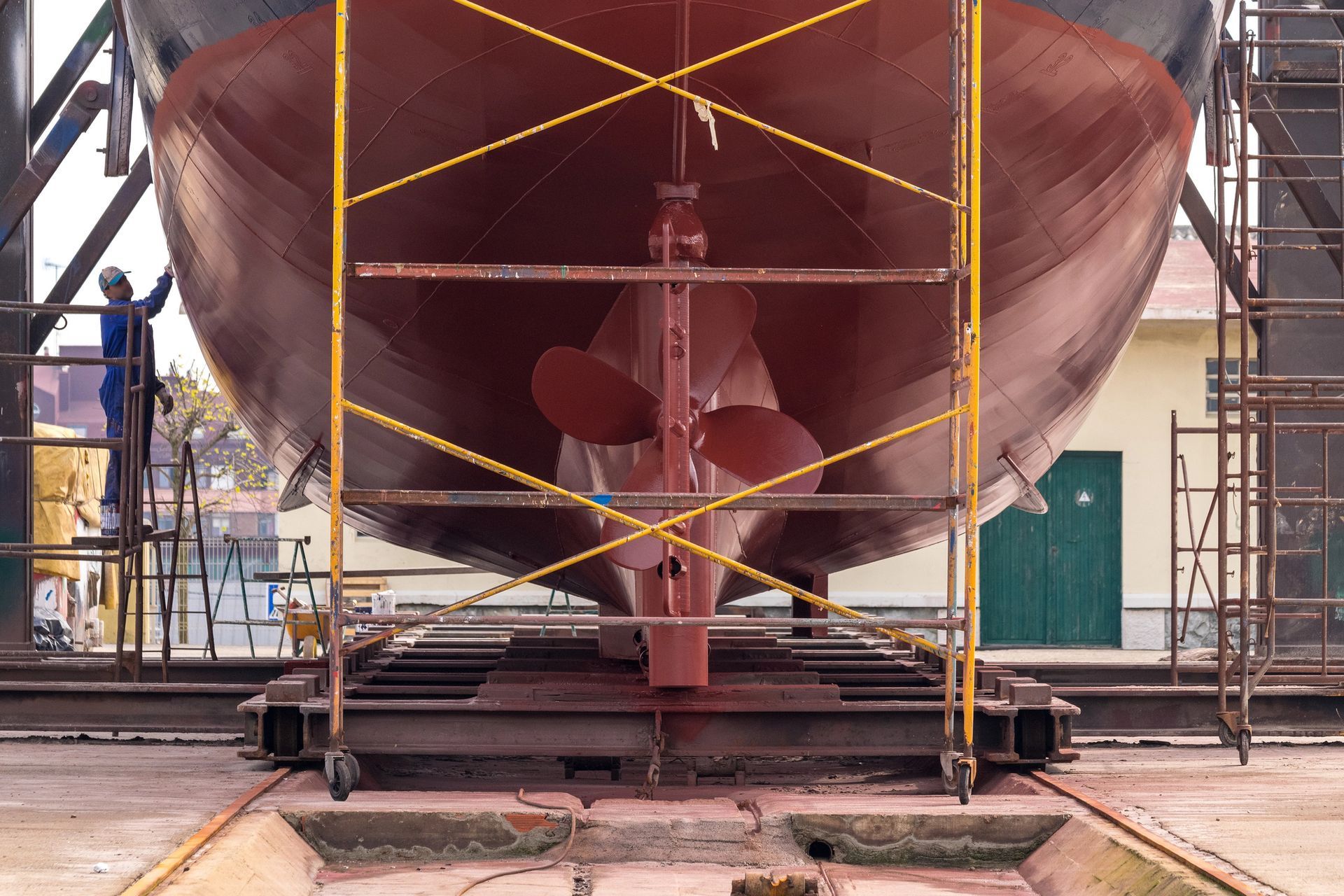 Scafo, elica e timone della nave in bacino di carenaggio per manutenzione; operaio su impalcatura.