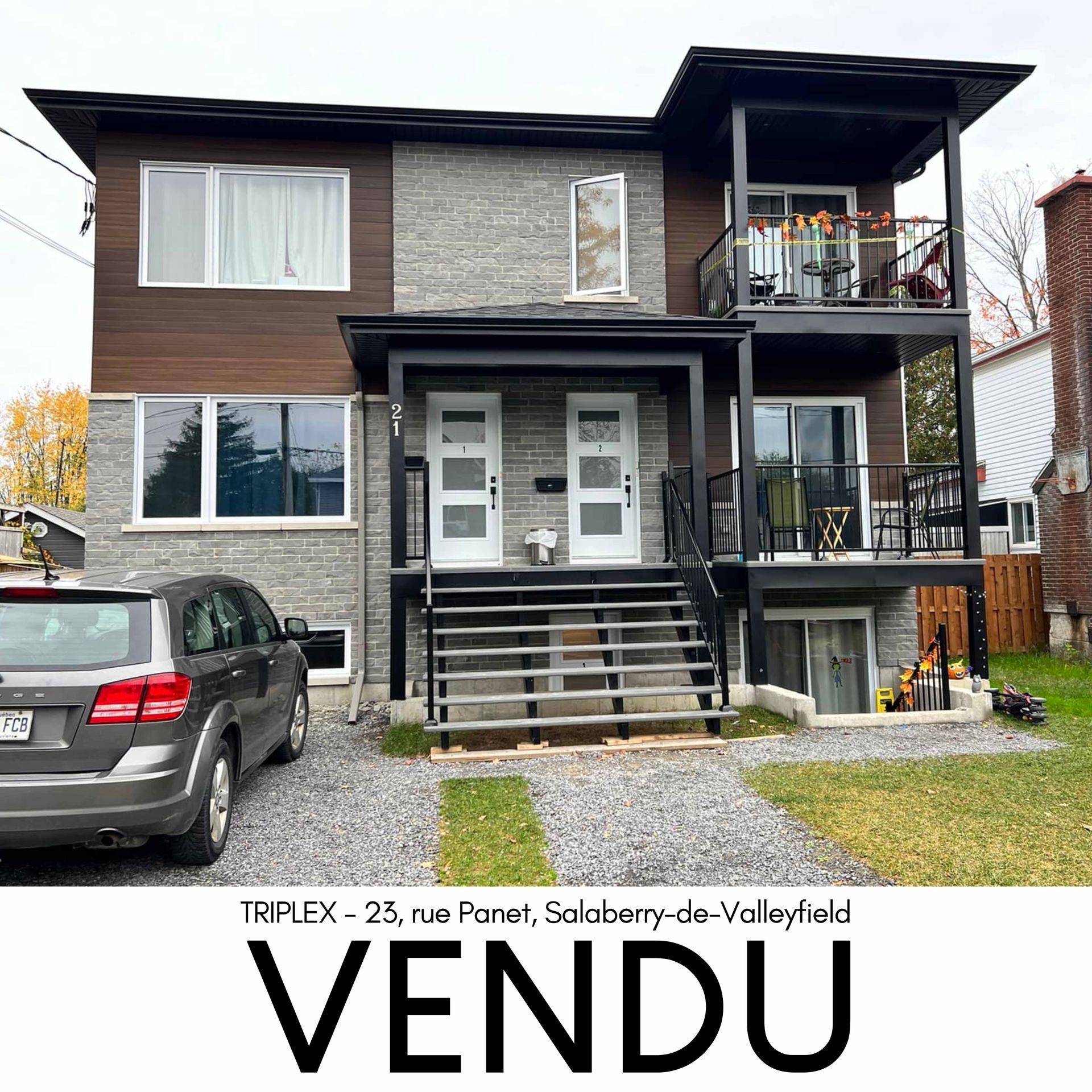 Triplex à vendre avec façade grise et brune et inscription « VENDU ». Comprend une voiture garée devant.