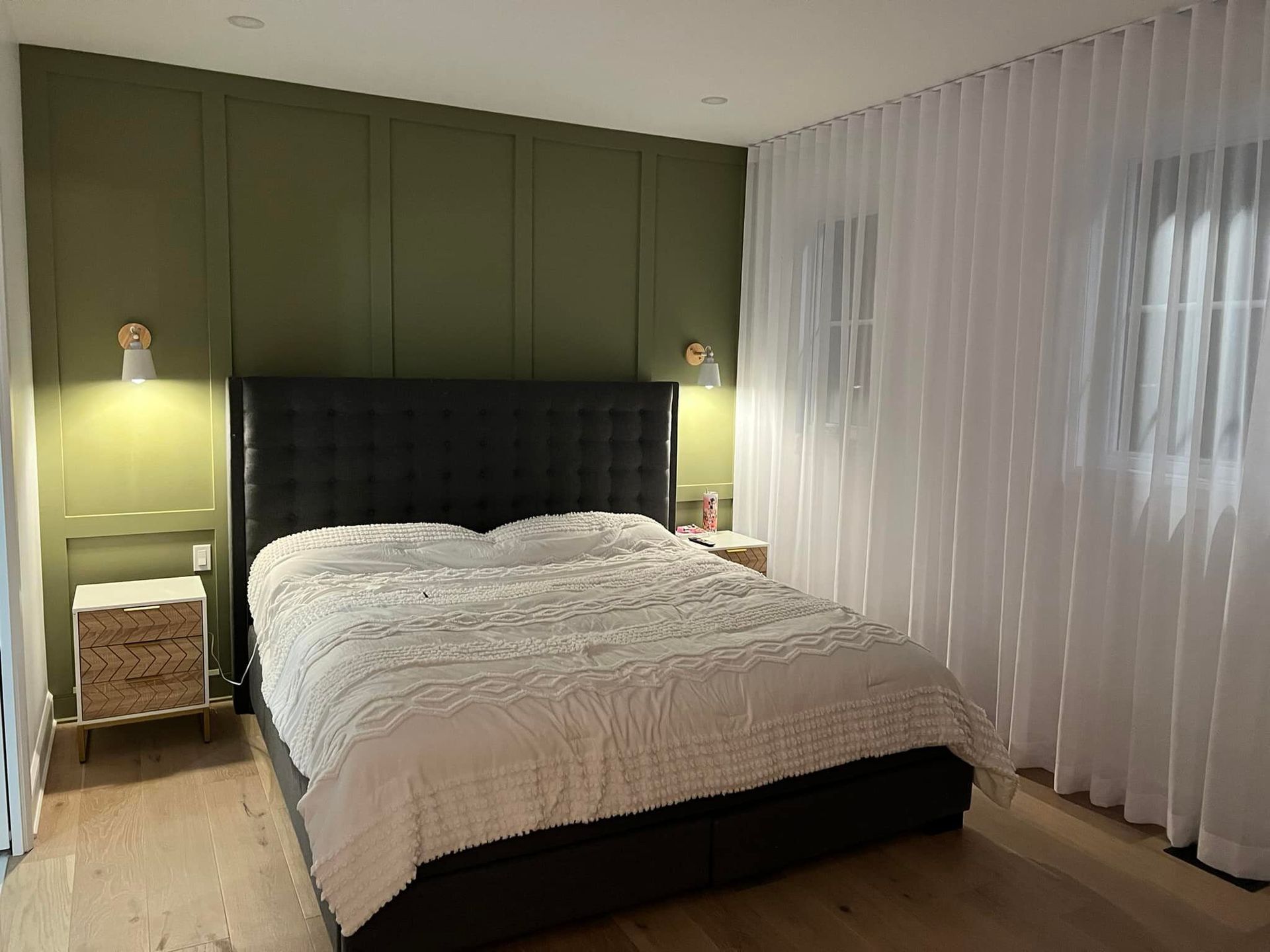 Une chambre avec un mur d'accent vert, un lit avec une literie blanche, deux tables de chevet et des rideaux blancs transparents.