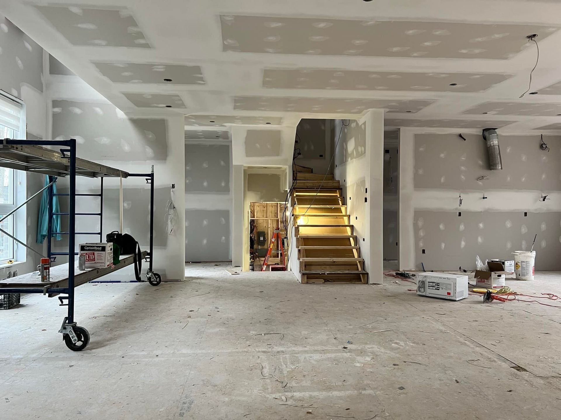 Chantier de construction intérieur avec cloisons sèches, escaliers non finis et échafaudage.