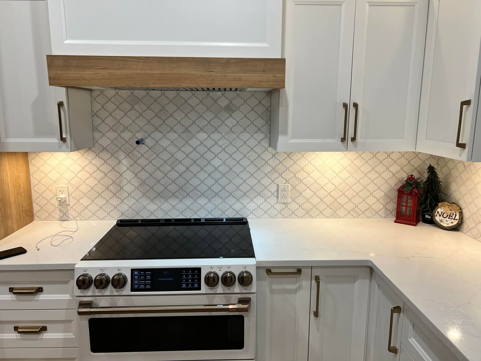 Cuisine blanche avec armoires blanches, crédence à motifs et cuisinière en acier inoxydable. On y retrouve également une hotte et des plans de travail en bois.