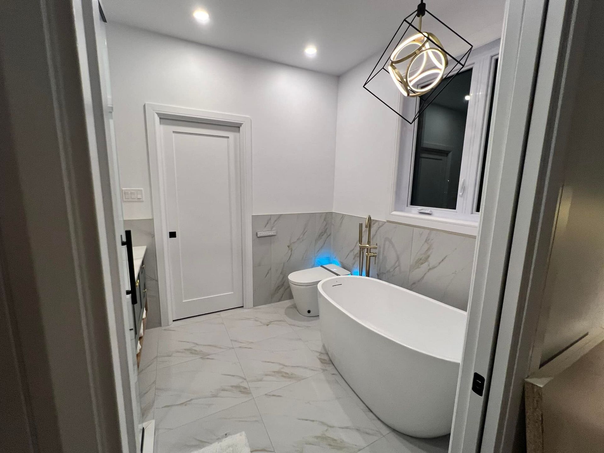 Salle de bain moderne avec baignoire autoportante blanche, carrelage aspect marbre et suspension géométrique.