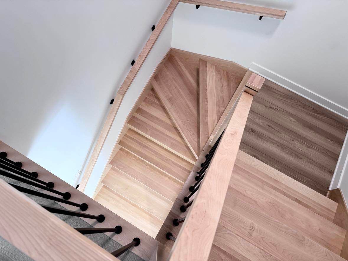 Escalier tournant en bois, vu de dessus. Marches et contremarches en bois clair, garde-corps noir.