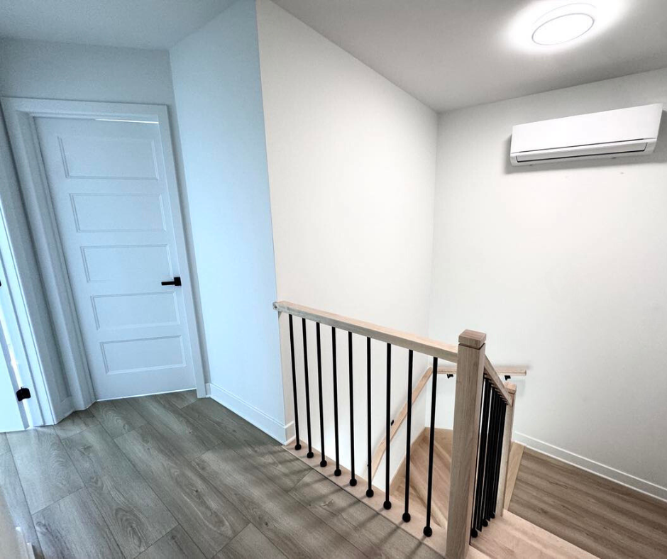 Couloir intérieur avec une porte blanche, un escalier avec une rampe noire et un climatiseur mural.