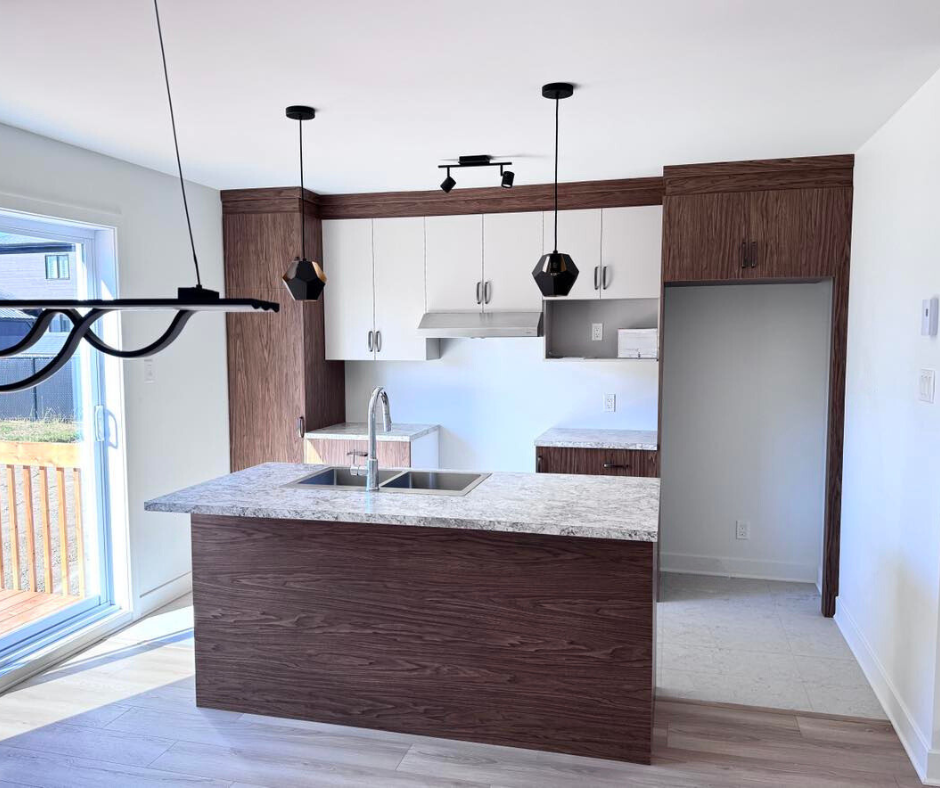 Cuisine moderne avec îlot et placards en bois foncé, meubles hauts blancs et suspensions. Une grande fenêtre se trouve à gauche.