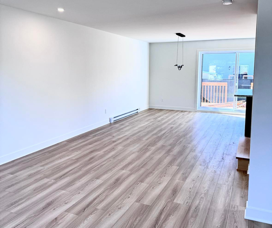 Salon vide avec parquet effet bois clair, murs blancs et porte coulissante menant à une terrasse.