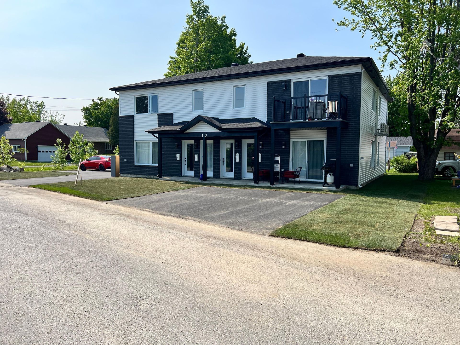 Immeuble d'appartements de deux étages avec façade blanche et noire. Allée en gravier devant, pelouse verte de chaque côté.