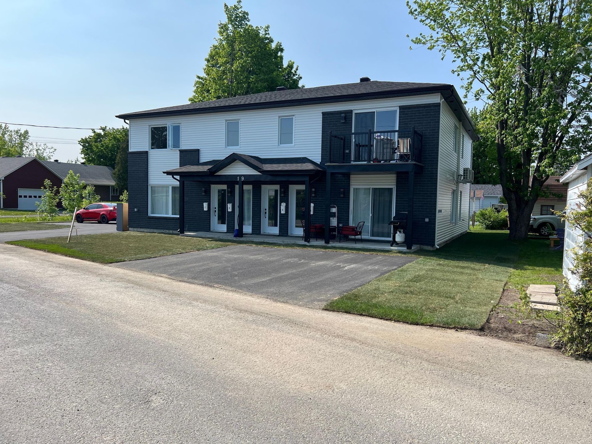 Immeuble d'appartements de deux étages avec façade noire et blanche. Allée en gravier gris devant. Gazon vert et arbres.