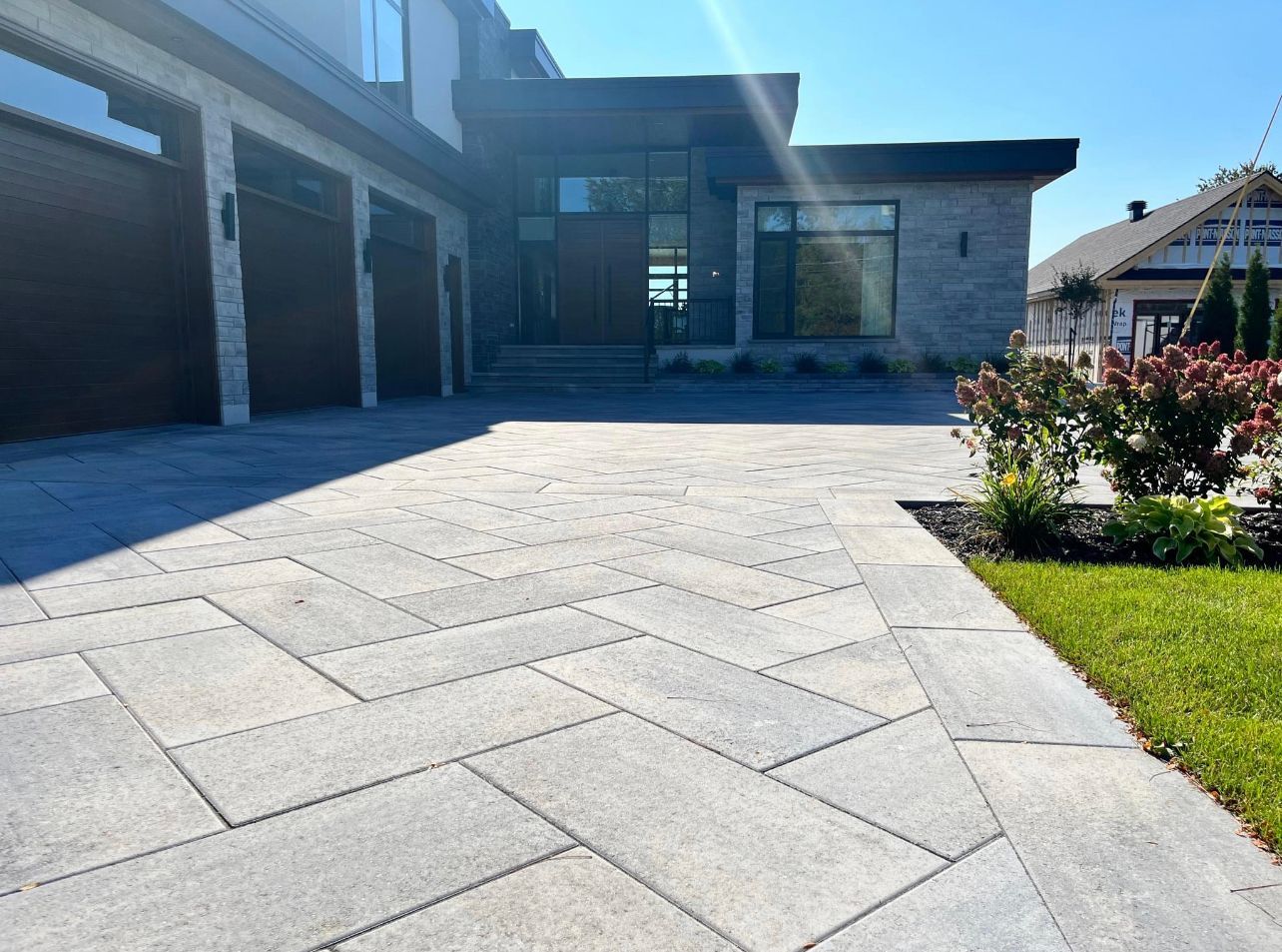 Allée d'une maison moderne avec façade en pierre. L'allée est pavée de blocs gris emboîtables.