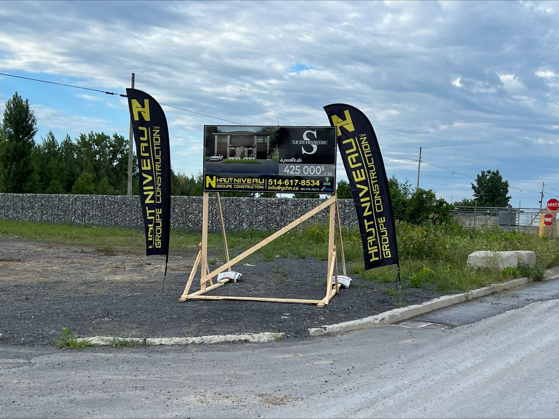 Panneau publicitaire de chantier, soutenu par un cadre en bois, avec deux drapeaux noirs.