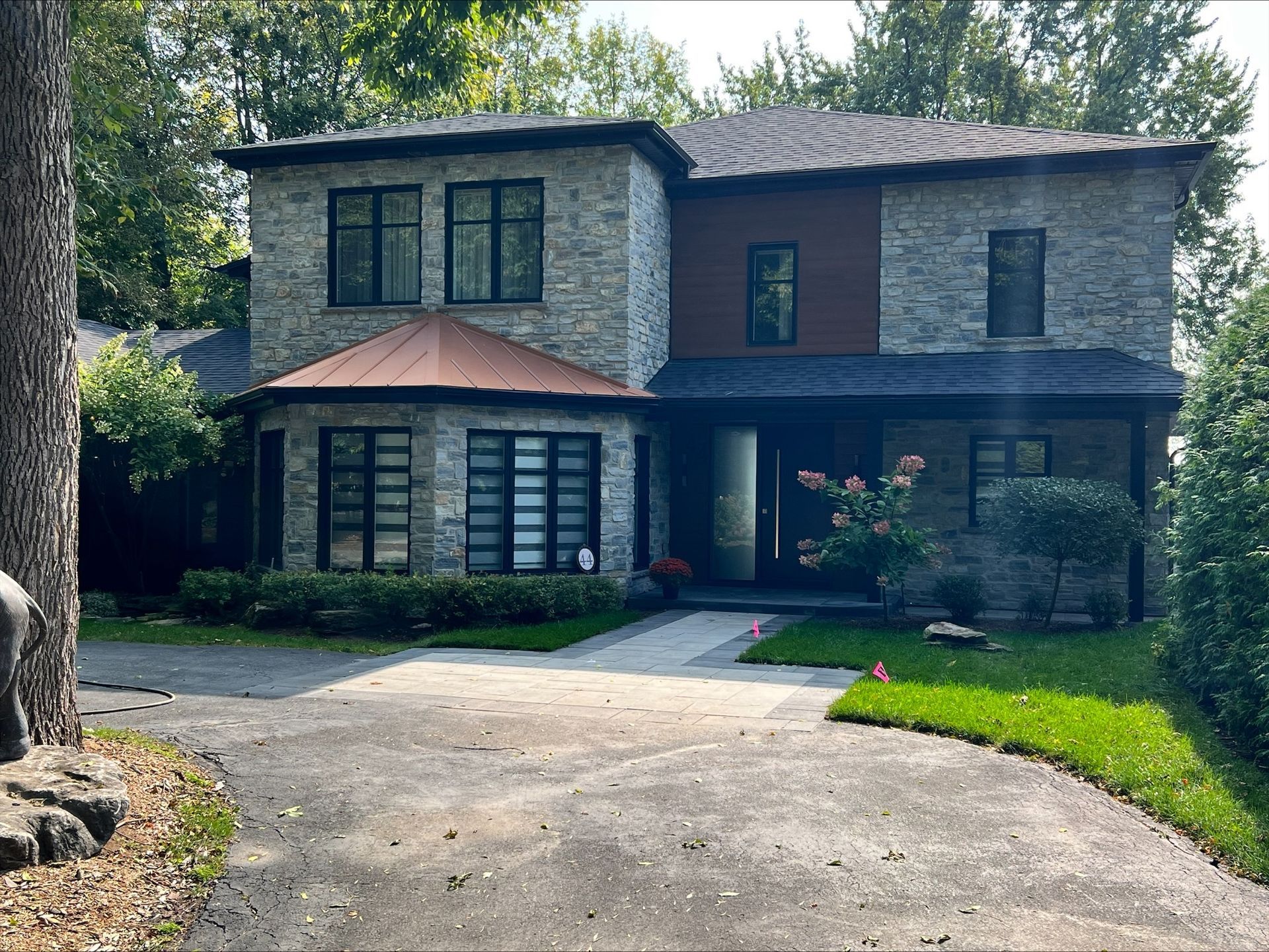 Maison de plain-pied en pierre, avec fenêtres aux boiseries sombres et touches cuivrées. Une allée pavée mène à la porte d'entrée, entourée de verdure.